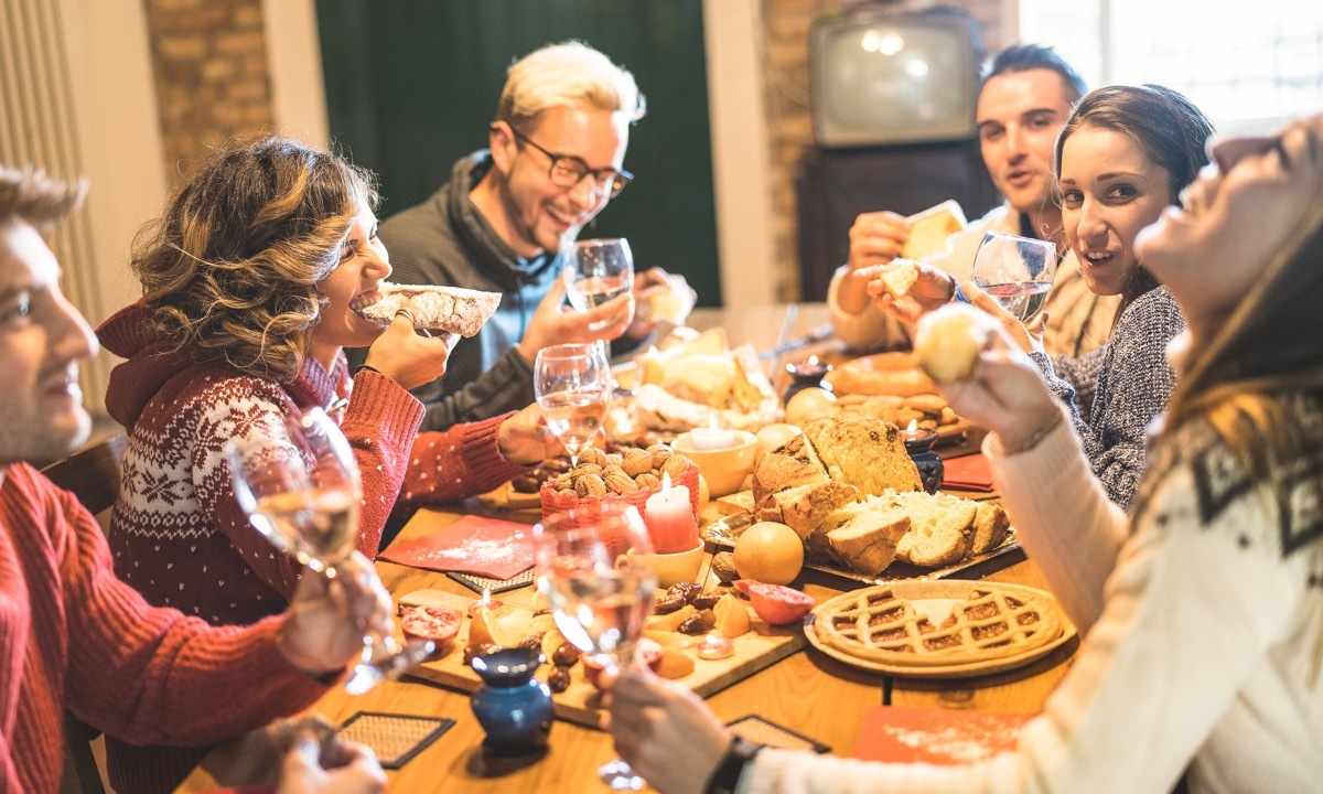 Front view of friends group tasting christmas sweets food and having fun at home drinking champagne sparkling wine - Winter holidays concept with people enjoying time eating together - Warm filter (Front view of friends group tasting christmas sweets