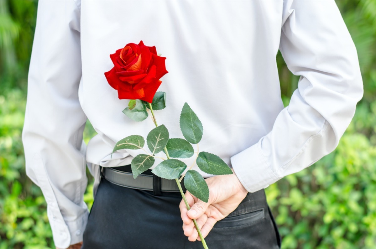 Man holding a red rose behind his back