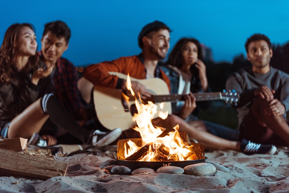 man playing guitar by campfire