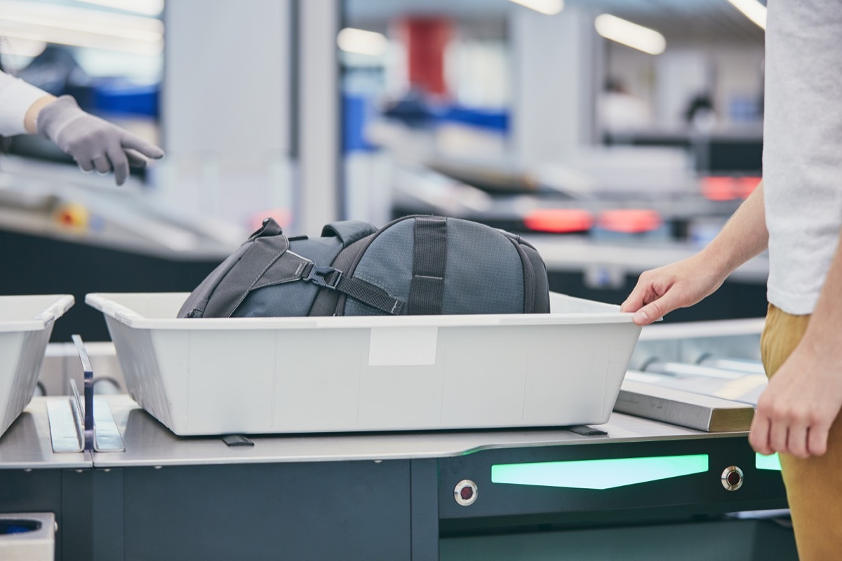 Airport security check. Young man (traveler) waiting for x-ray control his luggage.