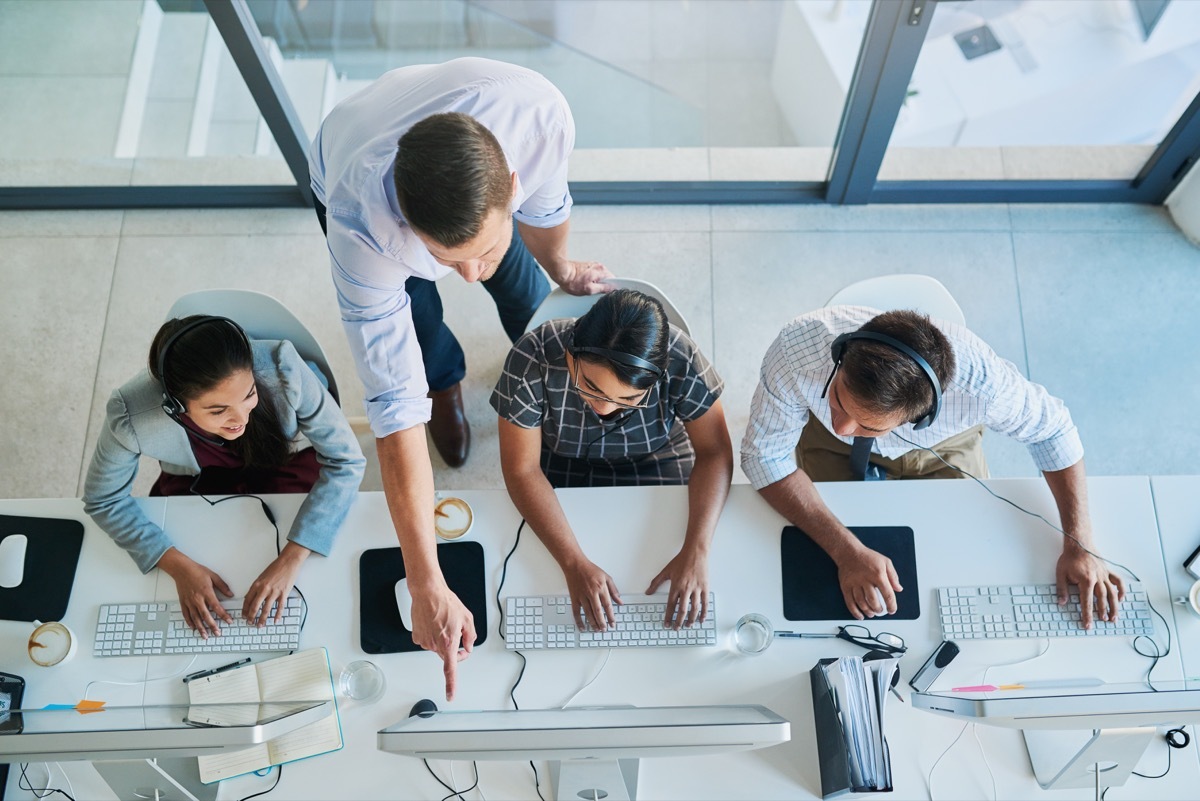 high angle shot of boss interacting with three employees on their computers