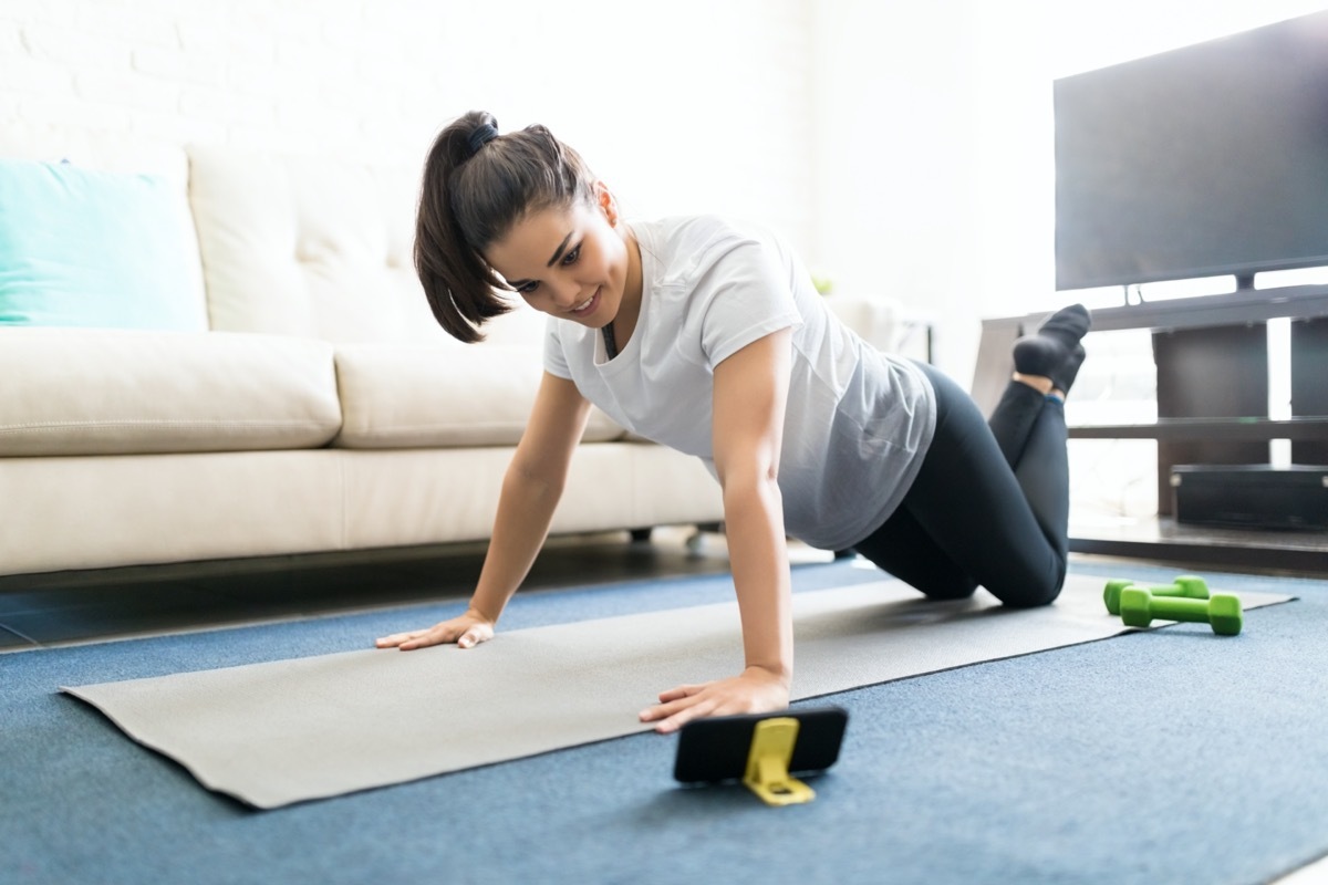 woman learning new exercises watching online workout tutorials over her phone at home