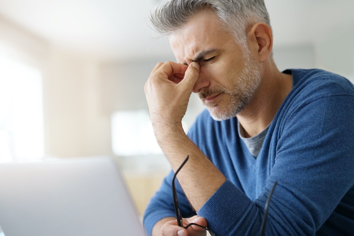 Man at home having a headache in front of laptop