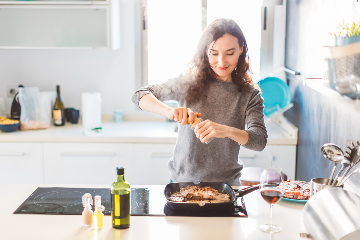 A woman adding spices to a dish while cooking