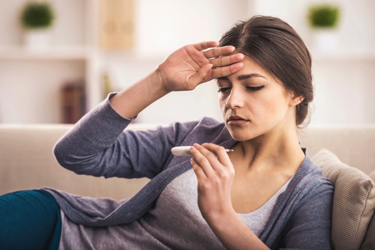 young white woman feeling her forehead and looking at a thermometer