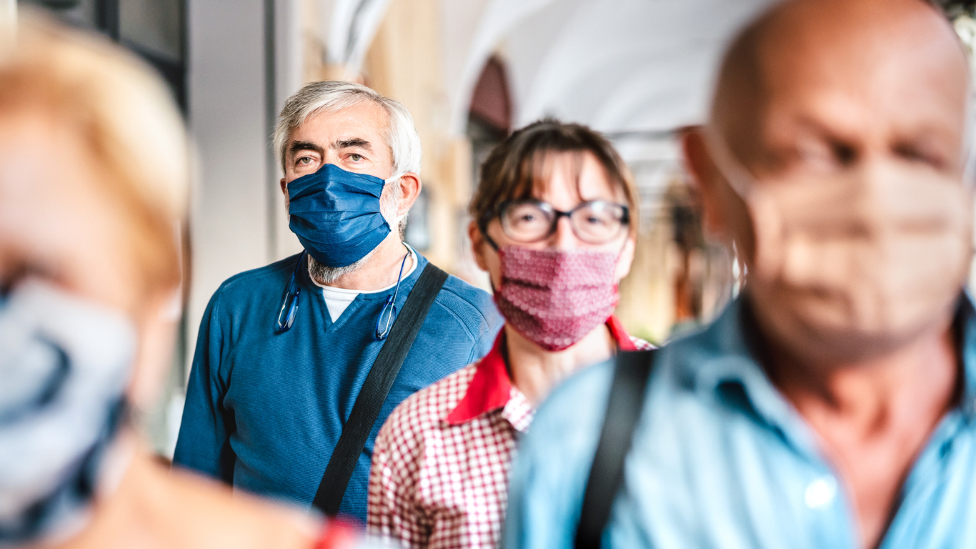 A crowd of people wearing face masks walk down a busy street in the city.