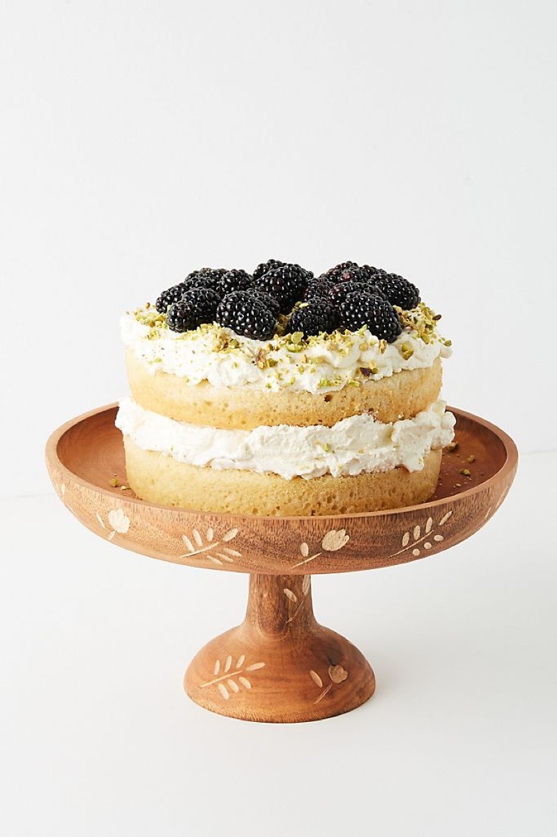 wooden cake stand with inlaid designs and cake with blackberries on it