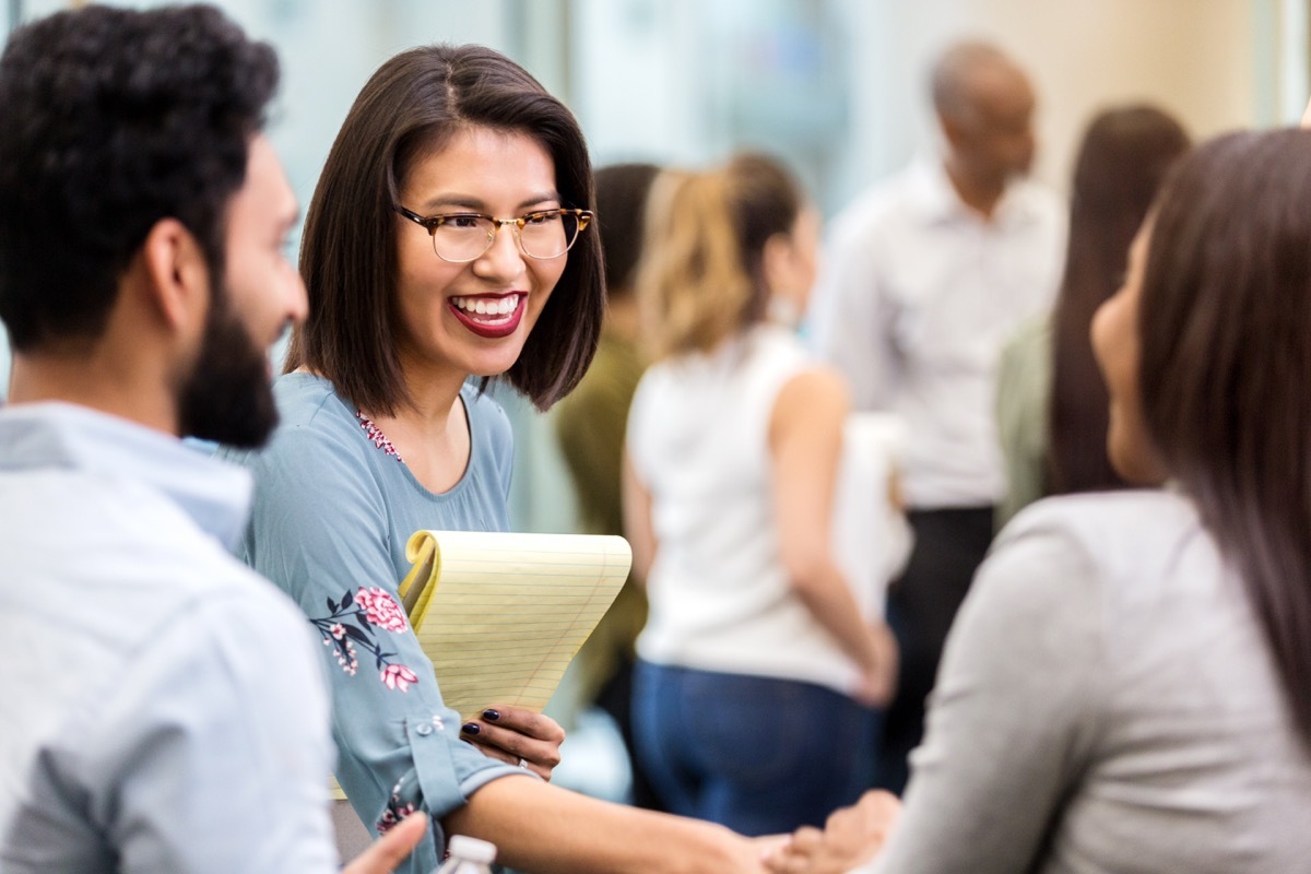 cheerful young businesswoman stands with an unrecognizable coworker in a crowded office building and smiles as she shakes hands with her new unrecognizable client