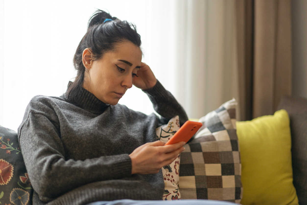 Woman sitting on a sofa and looking at mobile phone screen at home.