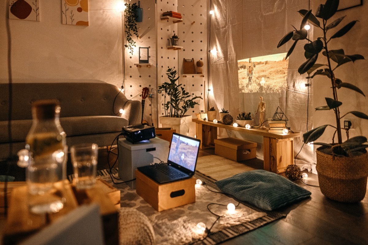 Empty living room with projector screen set up with couch and cushions and lights hanging on wall and floor