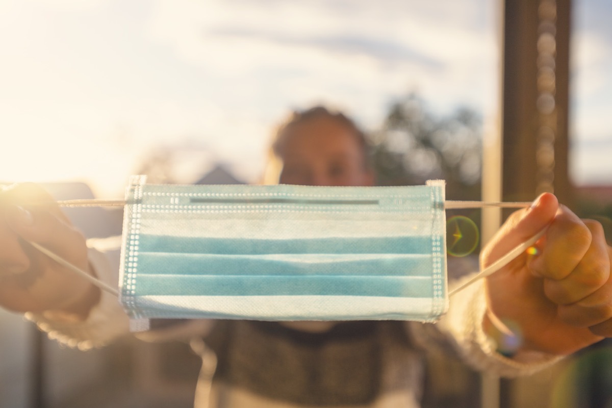 Woman holding out a surgical face mask. She is either about to put it on or is showing, or offering it to another person.