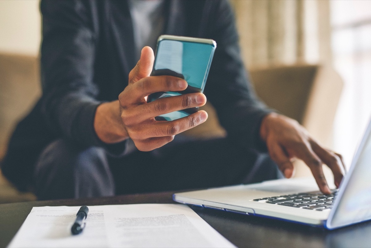 Cropped shot of an unrecognizable man using a smartphone and a laptop while working from home