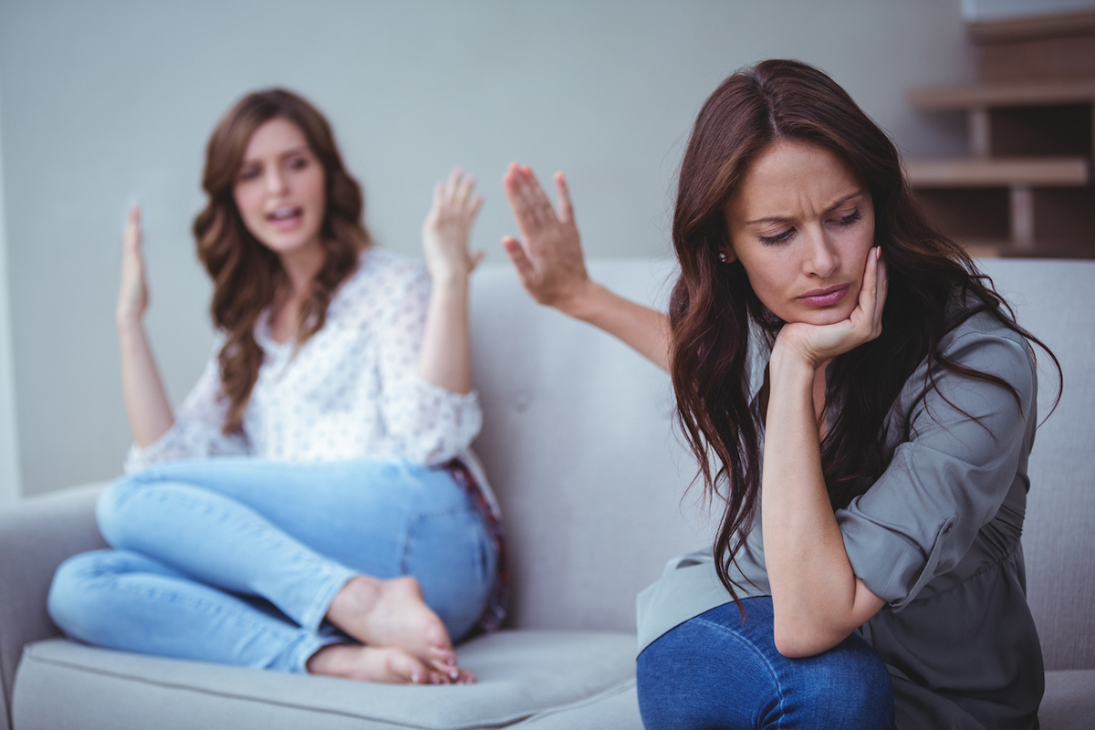 Two female friends sitting on sofa and arguing with each other