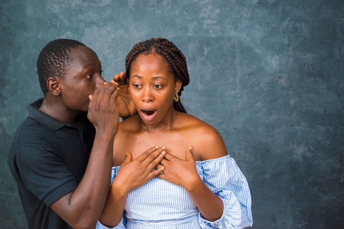 man whispering something to a woman who's shocked to hear it