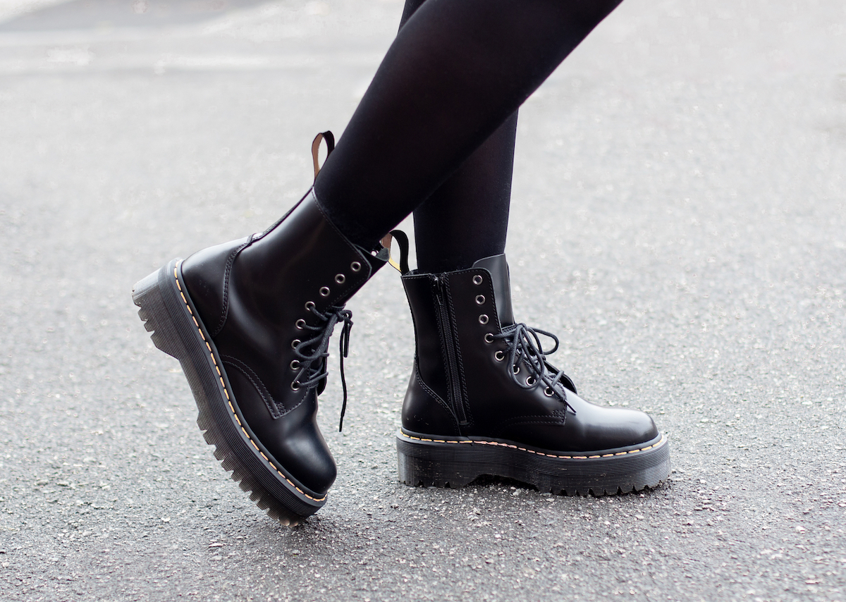 Female legs in black tights and black combat boots on a grey street background.