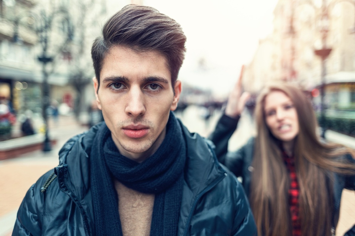 Young man turning back to his arguing girlfriend. Foreground focus on the male.