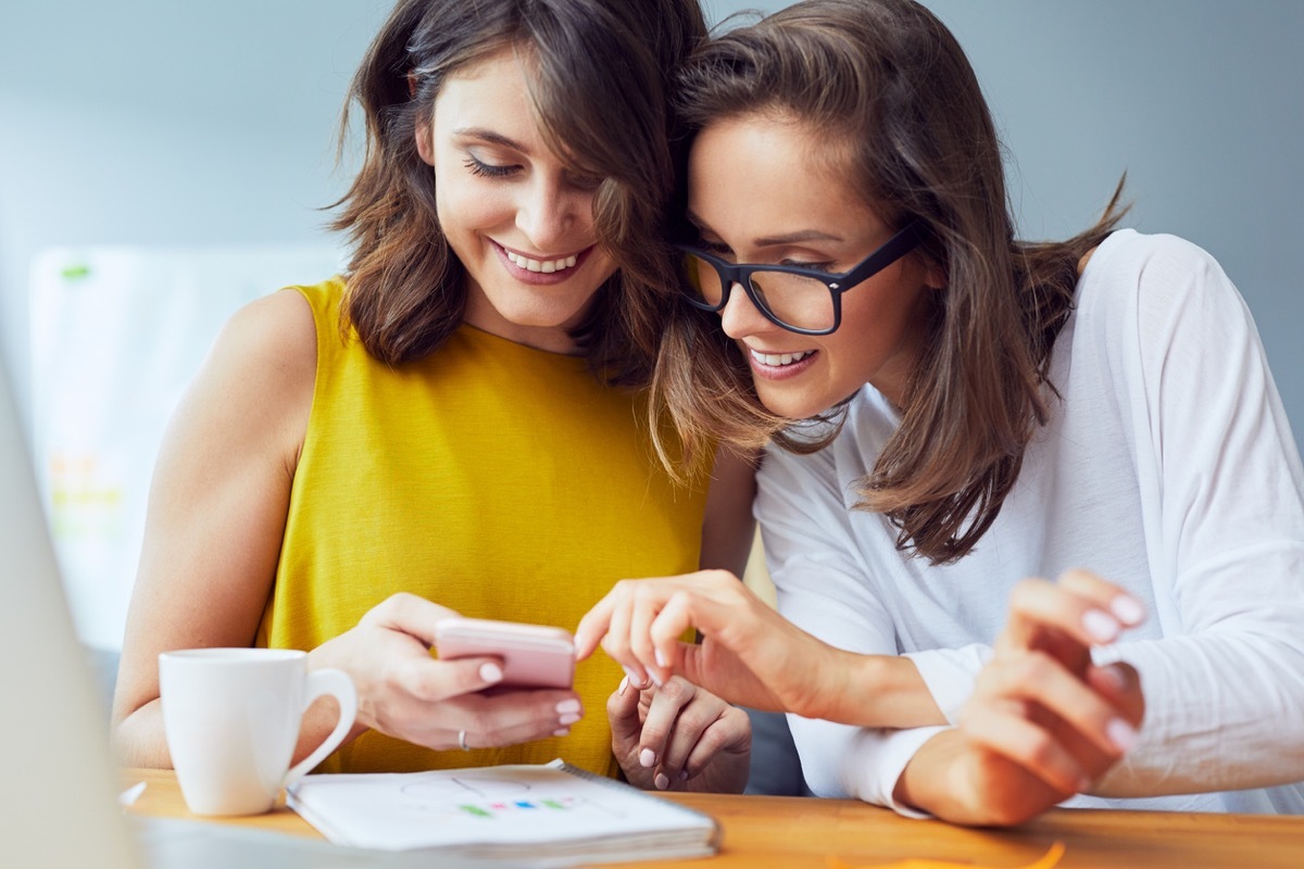 Female friends or lesbians browsing internet on mobile phone at work