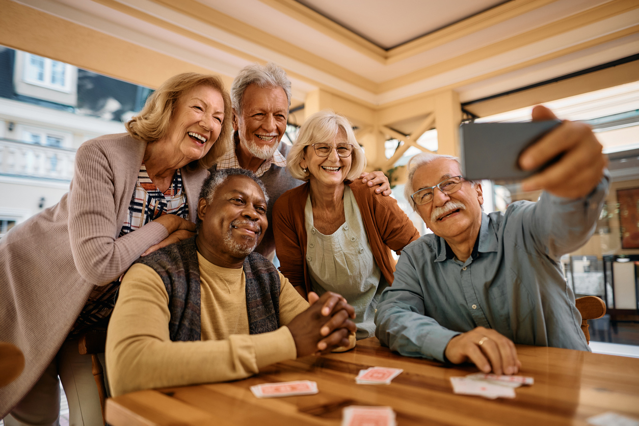 A group of five seniors taking a selfie in a retirement community lounge