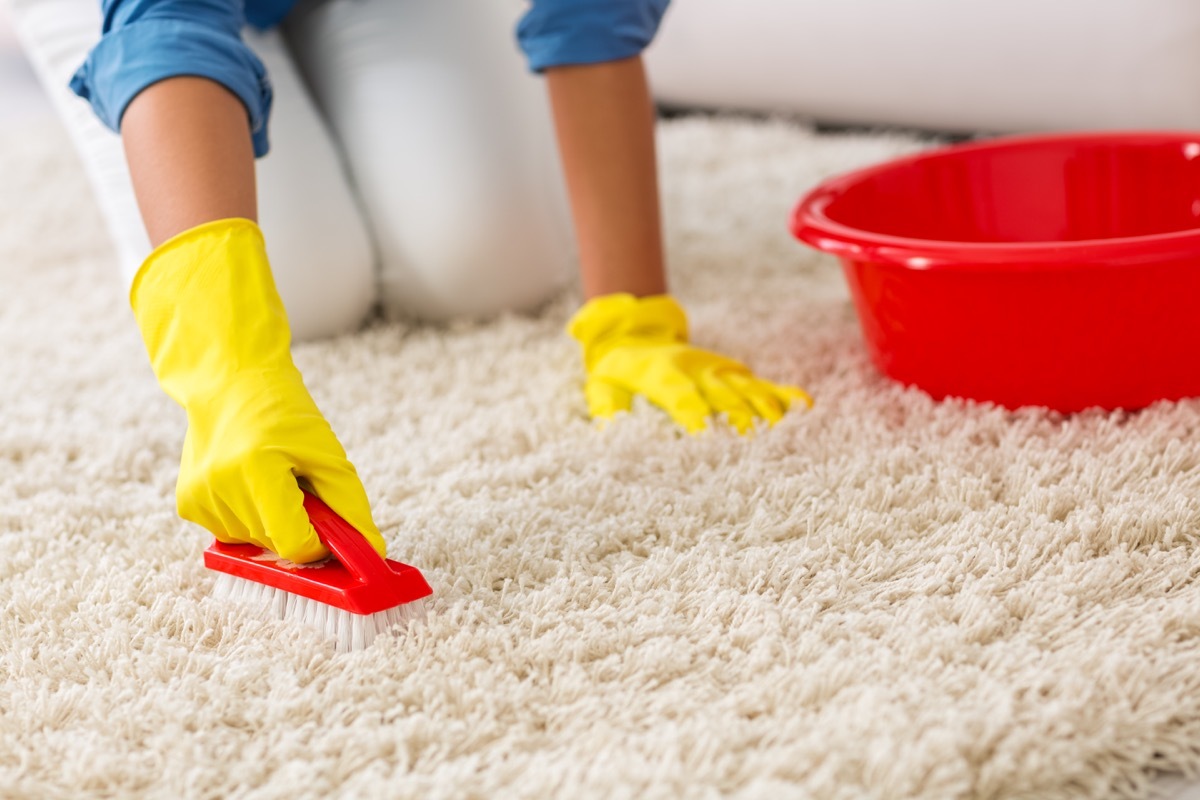 Woman washing carpet with brush at home