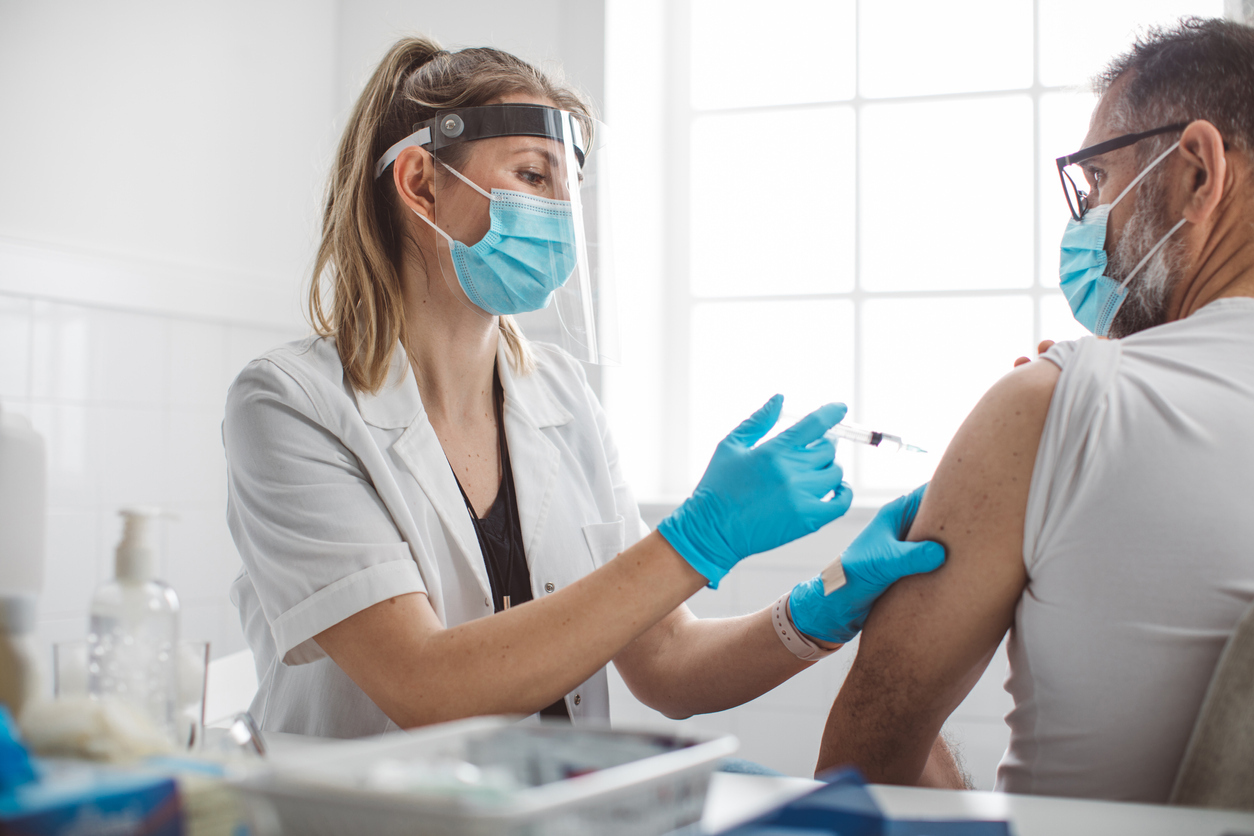 A young female nurse gives a middle-aged man a COVID vaccine in his arm.