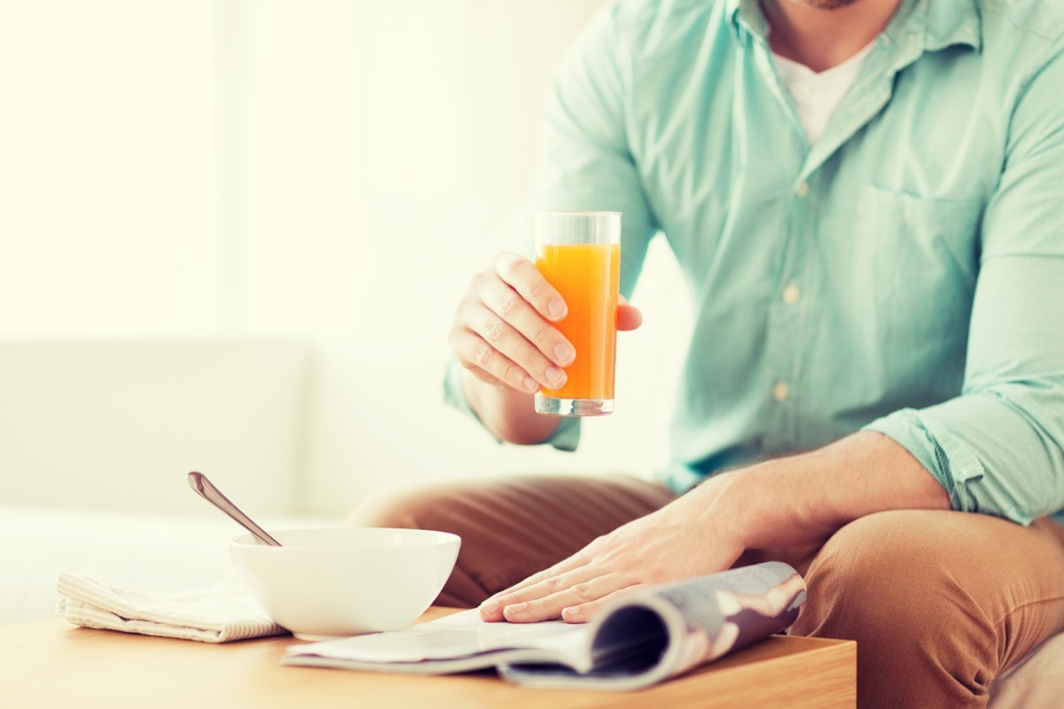 Man drinking fruit juice while he reads the paper and eats breakfast