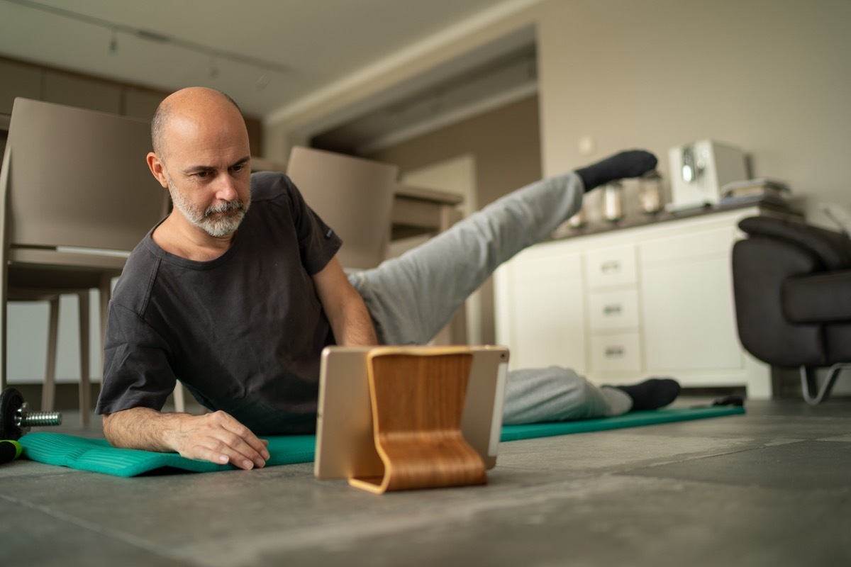 older white man exercising at home while looking at an ipad