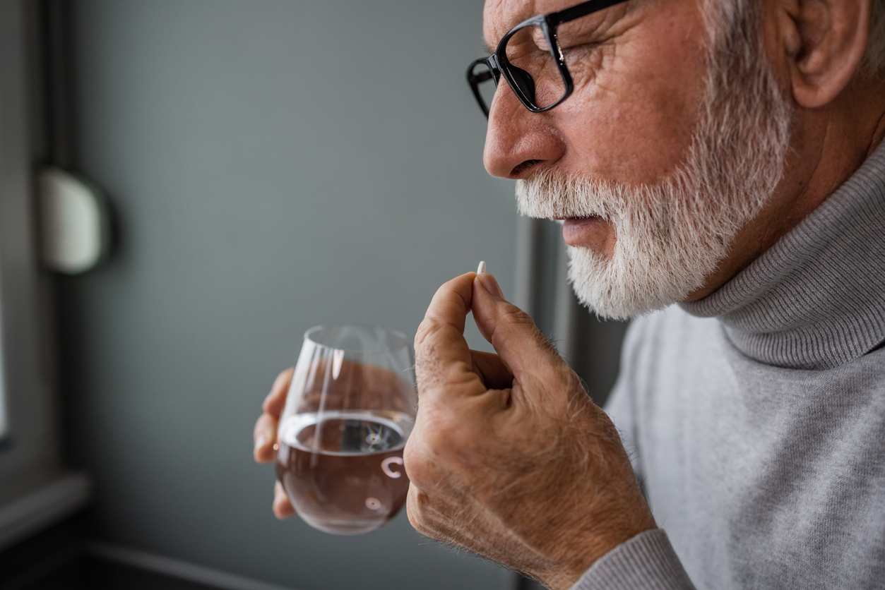 A senior man taking a supplement capsule with a glass of water