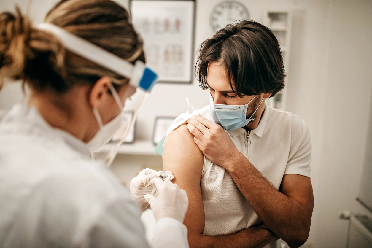 A young man rolling up his sleeve to receive a COVID vaccine booster shot