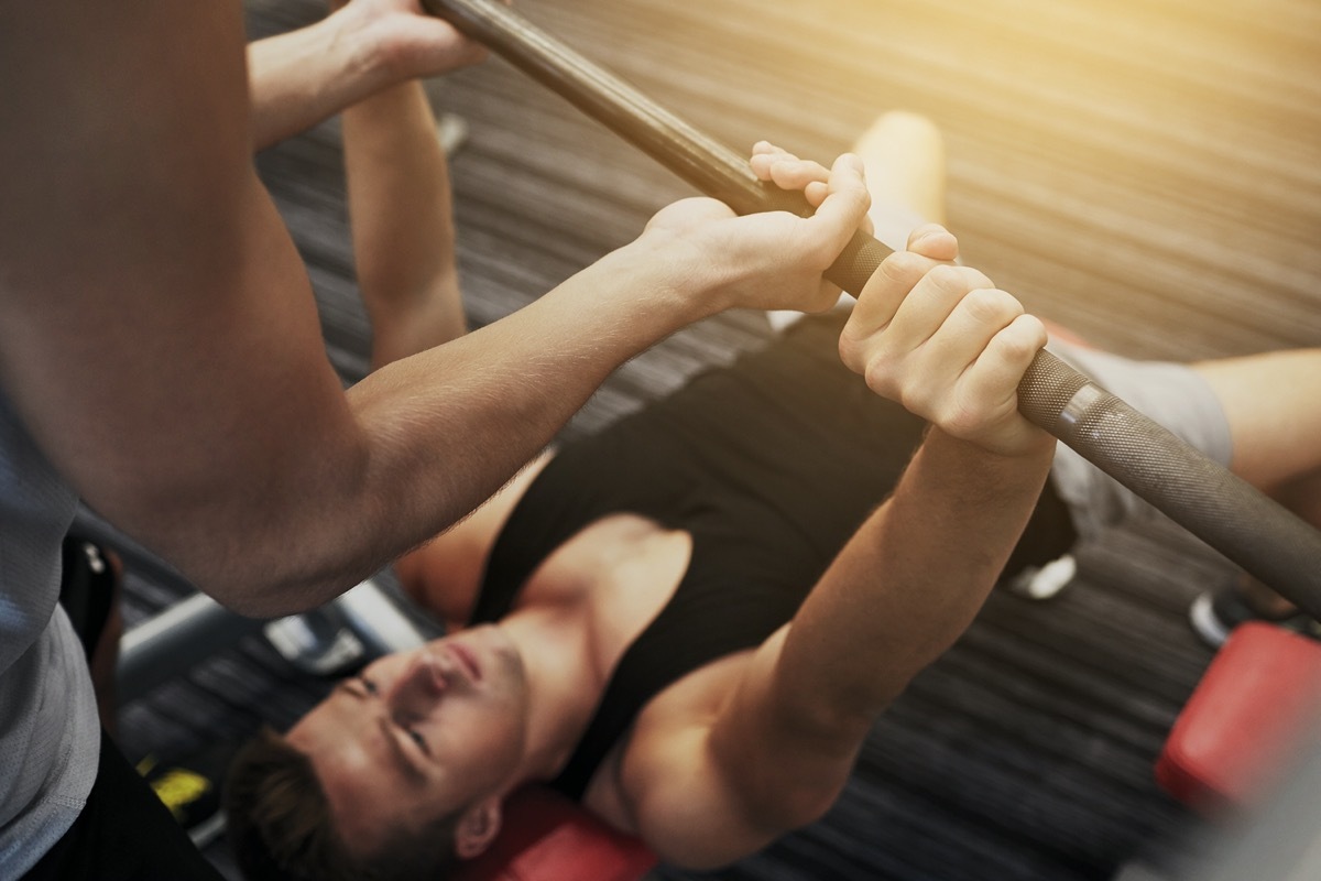 man and personal trainer with barbell flexing muscles in gym