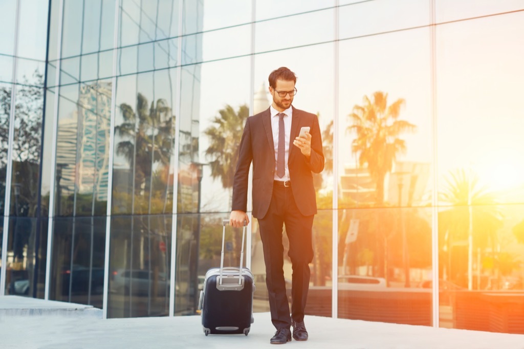 a man carrying a suitcase looks at his phone