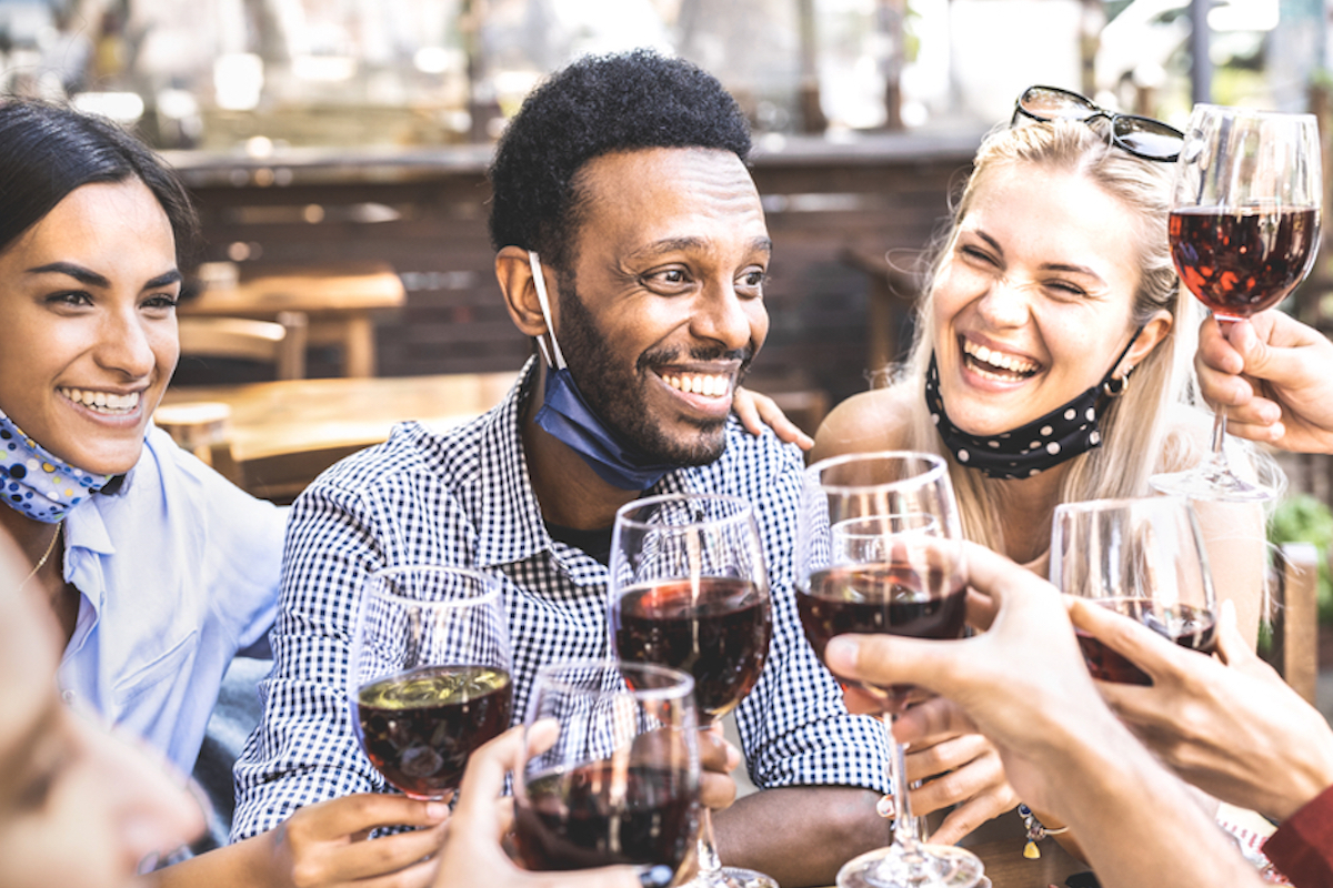 group of young people gather at barbecue drinking wine with masks under their chins