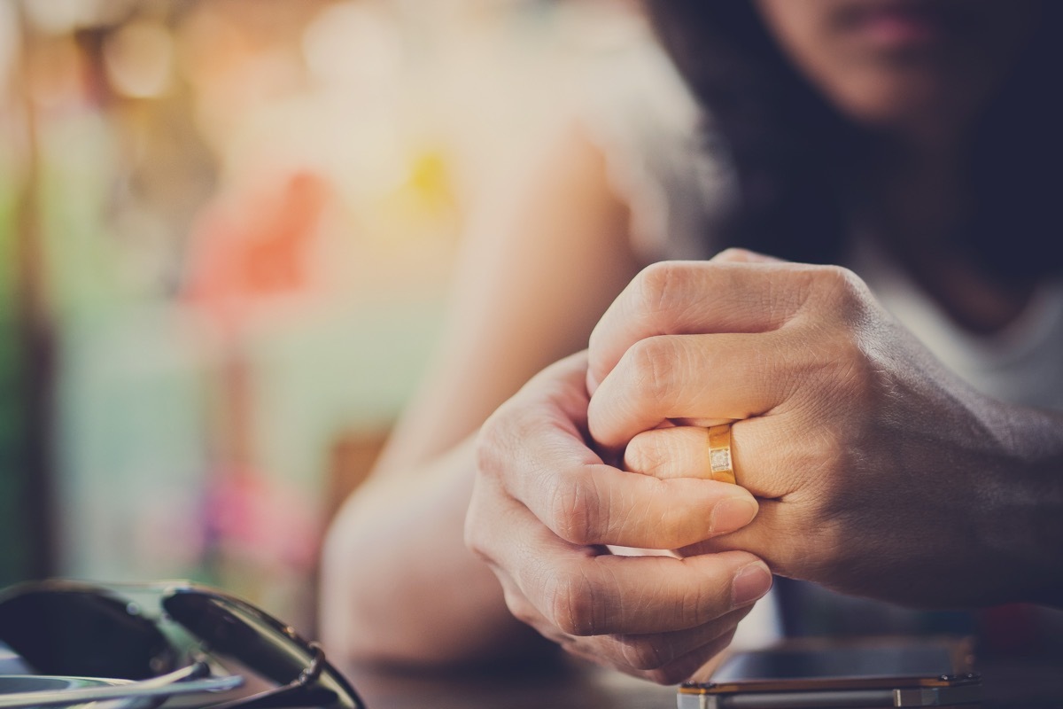 sad woman's hands clenched as she plays with wedding ring, married for money