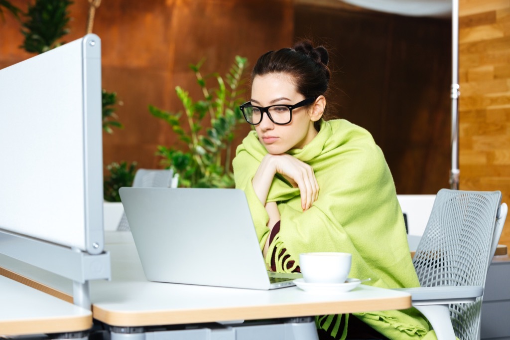 shivering woman in office with blanket, signs your cold is serious