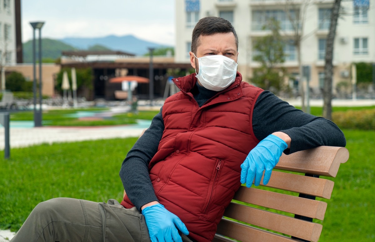 Man in a face mask sits on a bench and looks at the street