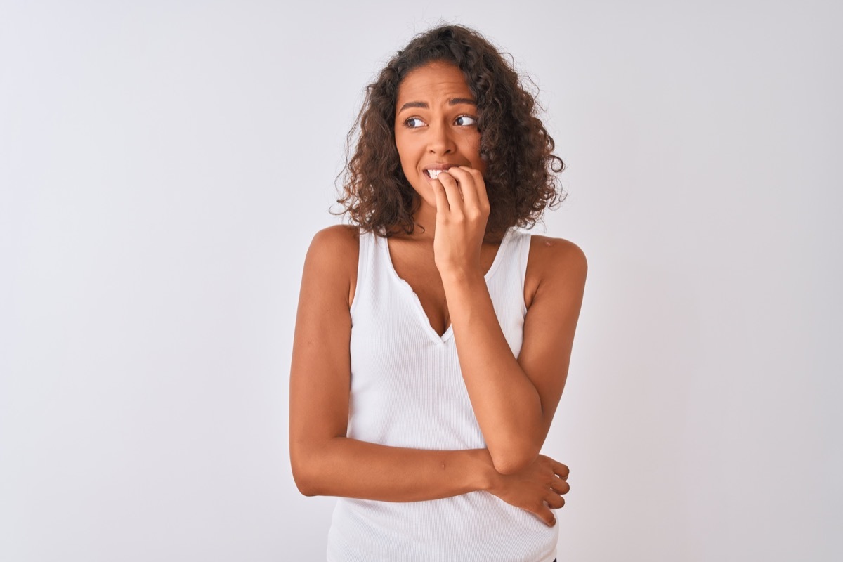 Young brazilian woman wearing casual t-shirt standing over isolated white background looking stressed and nervous with hands on mouth biting nails. Anxiety problem.