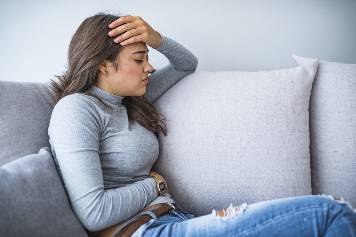 View of young woman suffering from stomachache on sofa at home