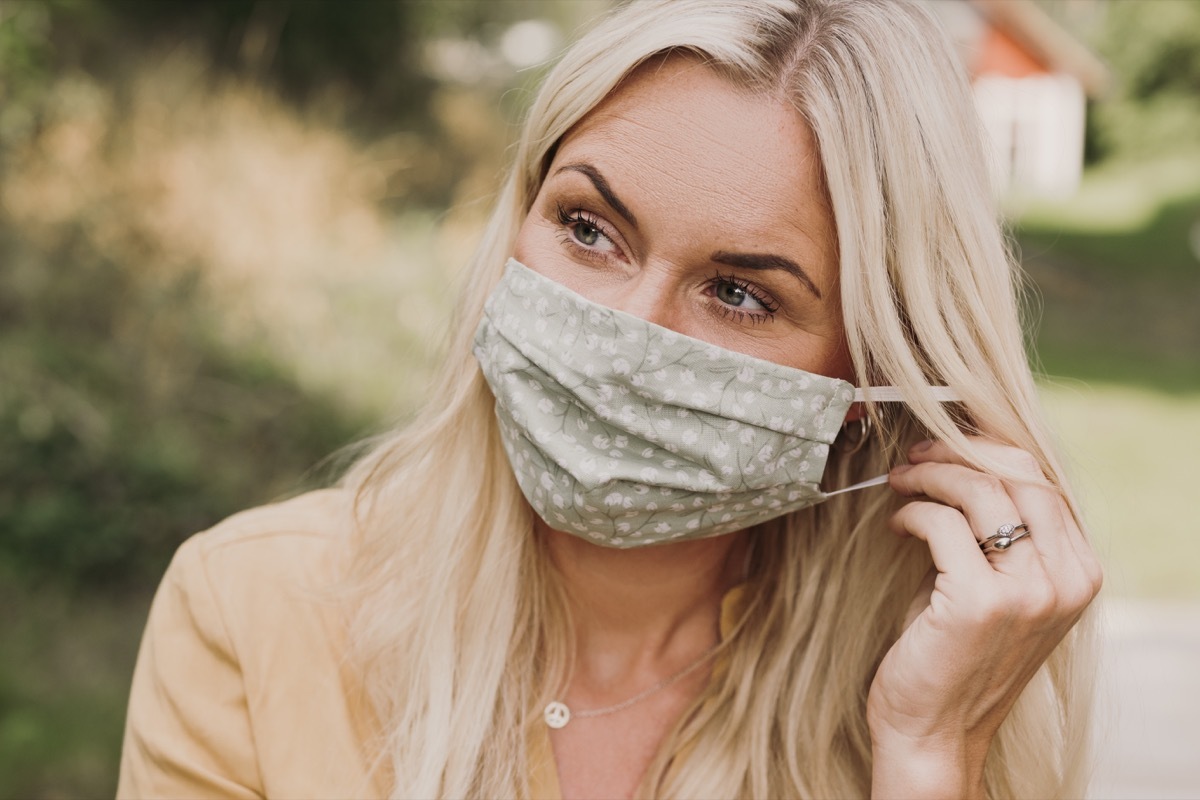 Content woman putting on wearing a protective mask in times of corona Mid adult woman earing a textiel mask with pocket for filter Photo taken outdoors in summer