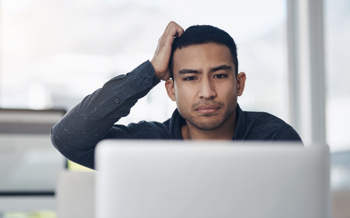 young businessman sitting alone in his office and looking confused while using his laptop