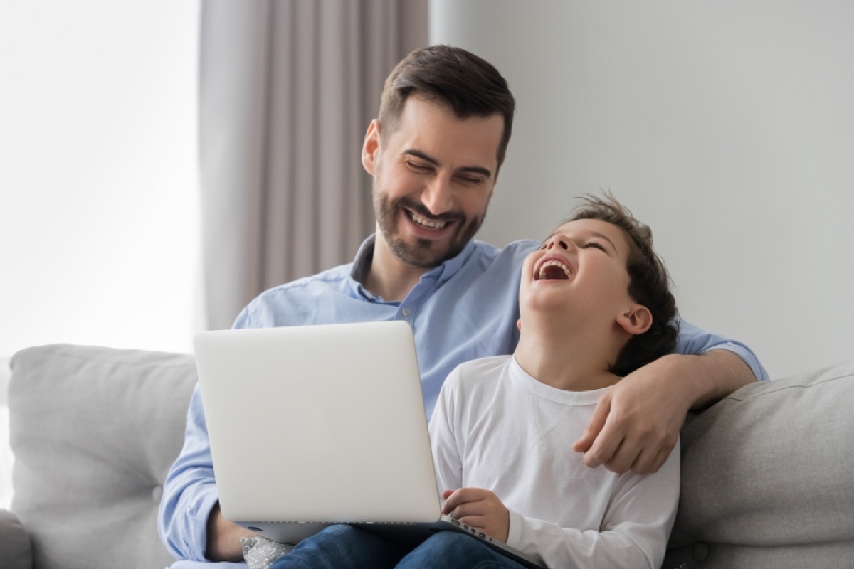 dad jokes - father and son looking at a computer screen and laughing on a couch