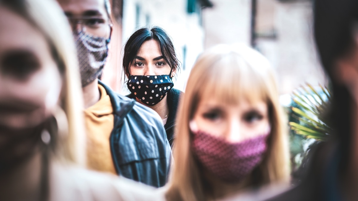 commuter crowd of people moving on city street covered by face mask - New normal human condition and society concept - Focus on middle woman wearing black facemask - Desaturated contrast filter