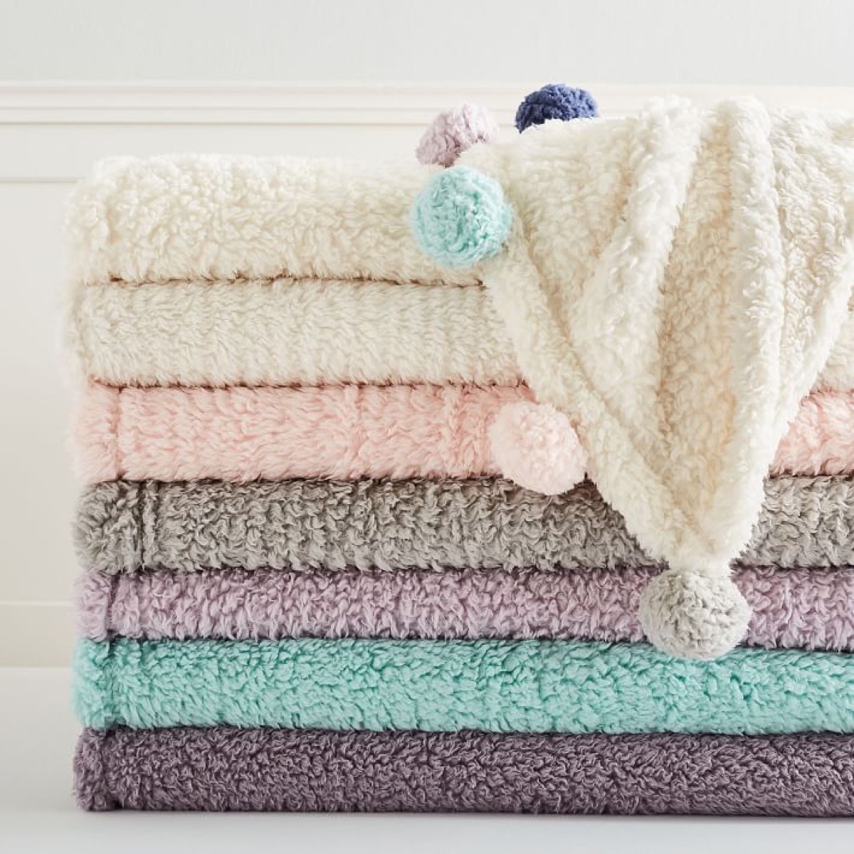 stack of fuzzy throws with pom pom trim