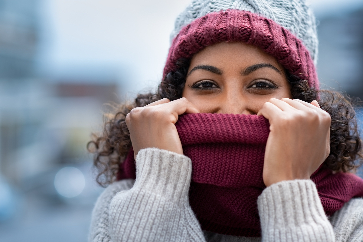 Closeup of woman holding woolen scarf with hands over nose