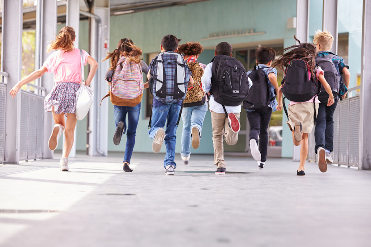 group of kids running into school, photo taken from behind