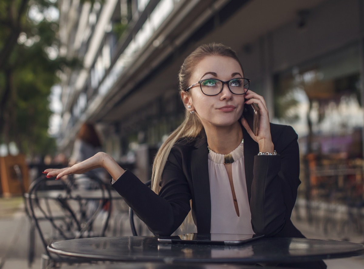 Woman on the Phone Rolling Her Eyes while sitting outside at a cafe table