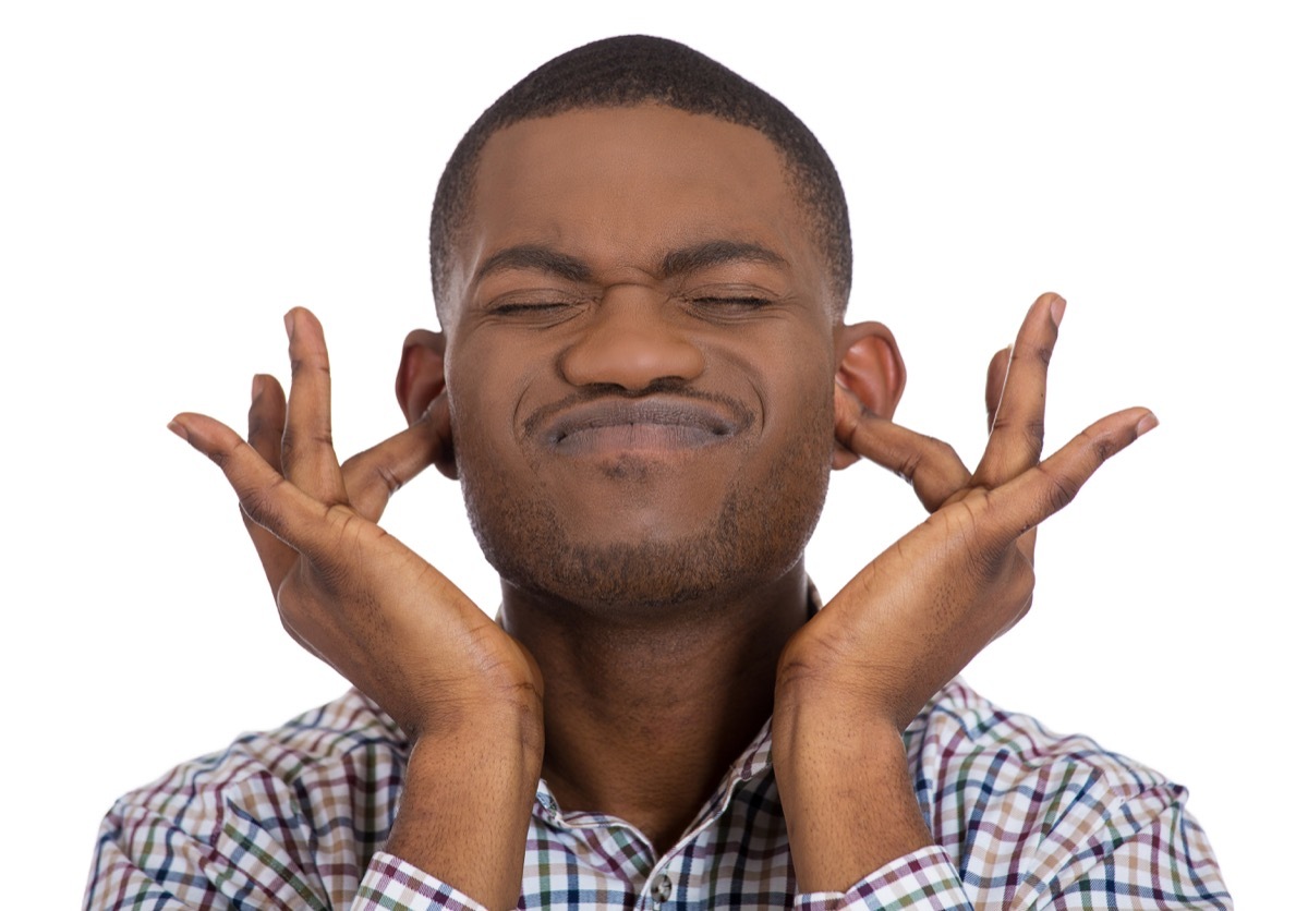 Black man puts fingers in his ears because he does not want to listen, check hearing to be a healthier man