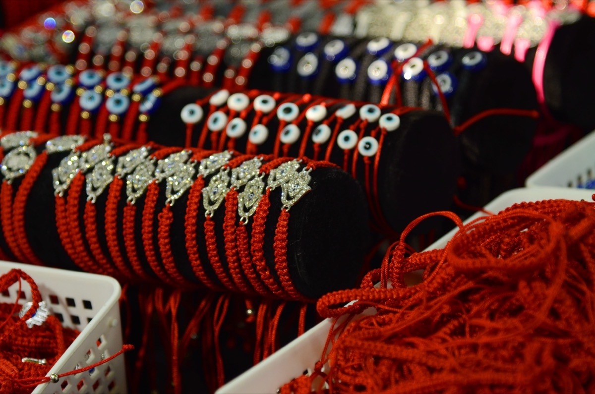 Braided red thread bracelet on the wrist of Israel. Symbol, amulet against the evil eye. Display case with decorations at the Carmel market in Tel Aviv. Souvenir from the holy land.