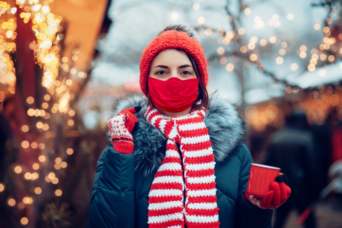 woman drinking punch on christmas market wearing medicine mask.