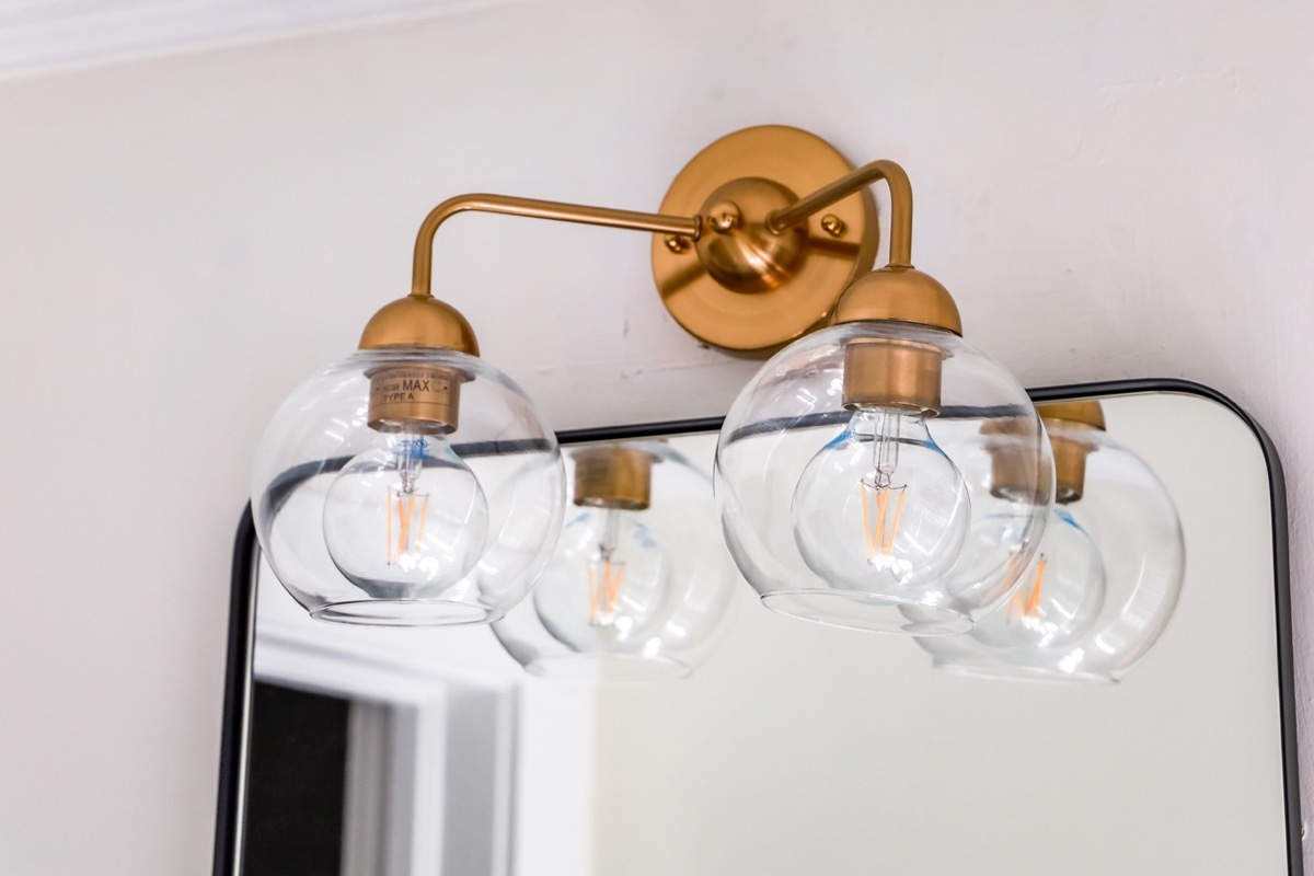 A clear glass double lighht ficture with gold brass accents in a small guest bathroom on top of a black rimmed retro style mirror.