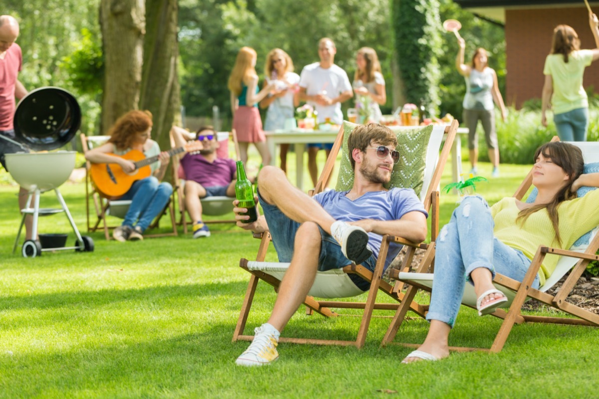 Young friends having barbecue picnic in the nature, playing guitar, playing badminton, enjoying sunny summer day outdoor