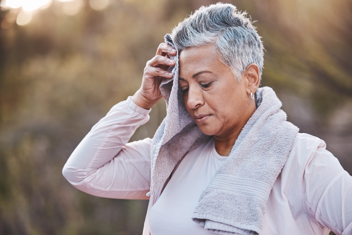 Gray-haired woman in a long-sleeve pink top sweating after an outdoor workout